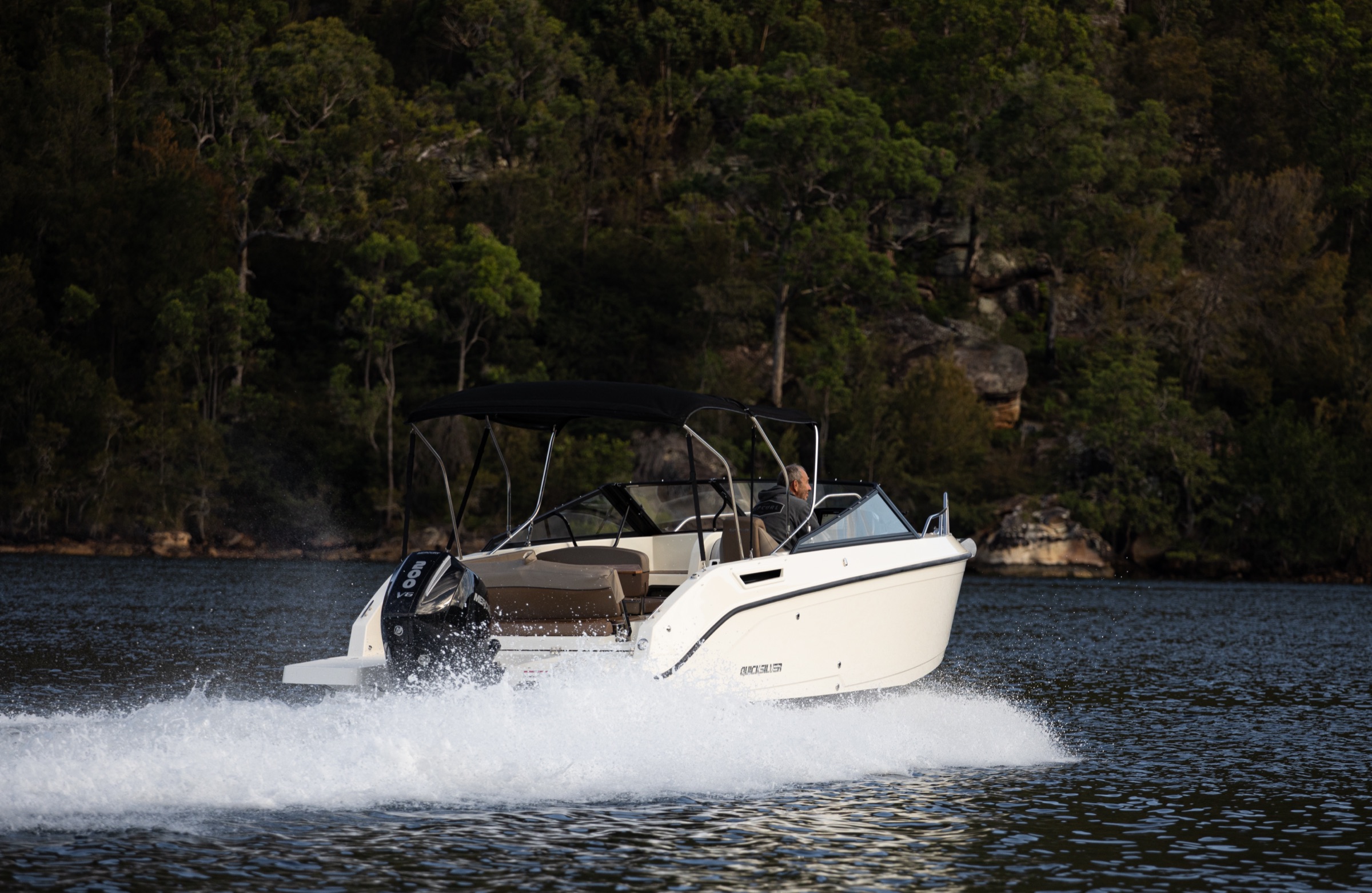 Boat underway with wake in bushland setting